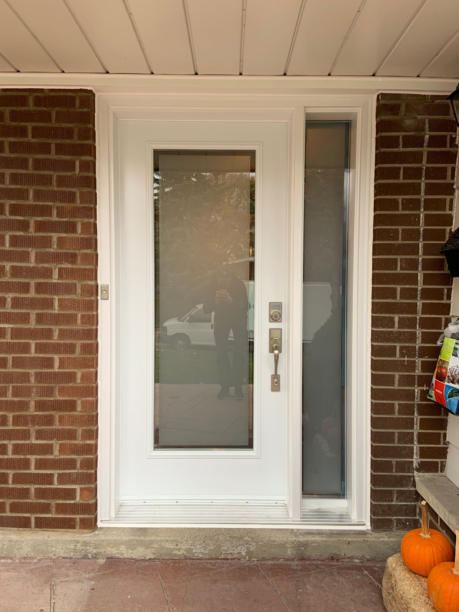 A white door is on a brick wall next to pumpkins.