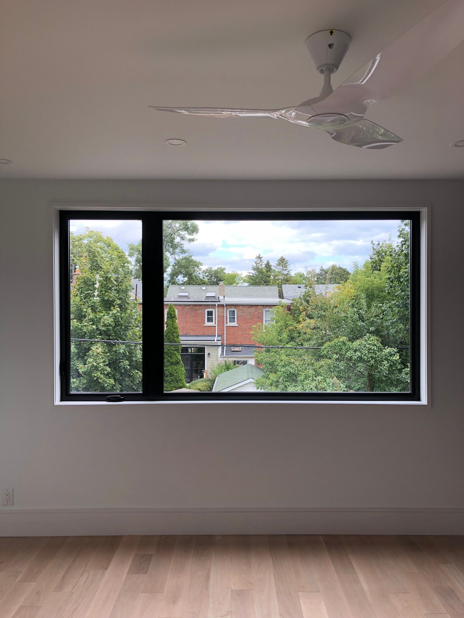 An empty room with a large window and a ceiling fan.