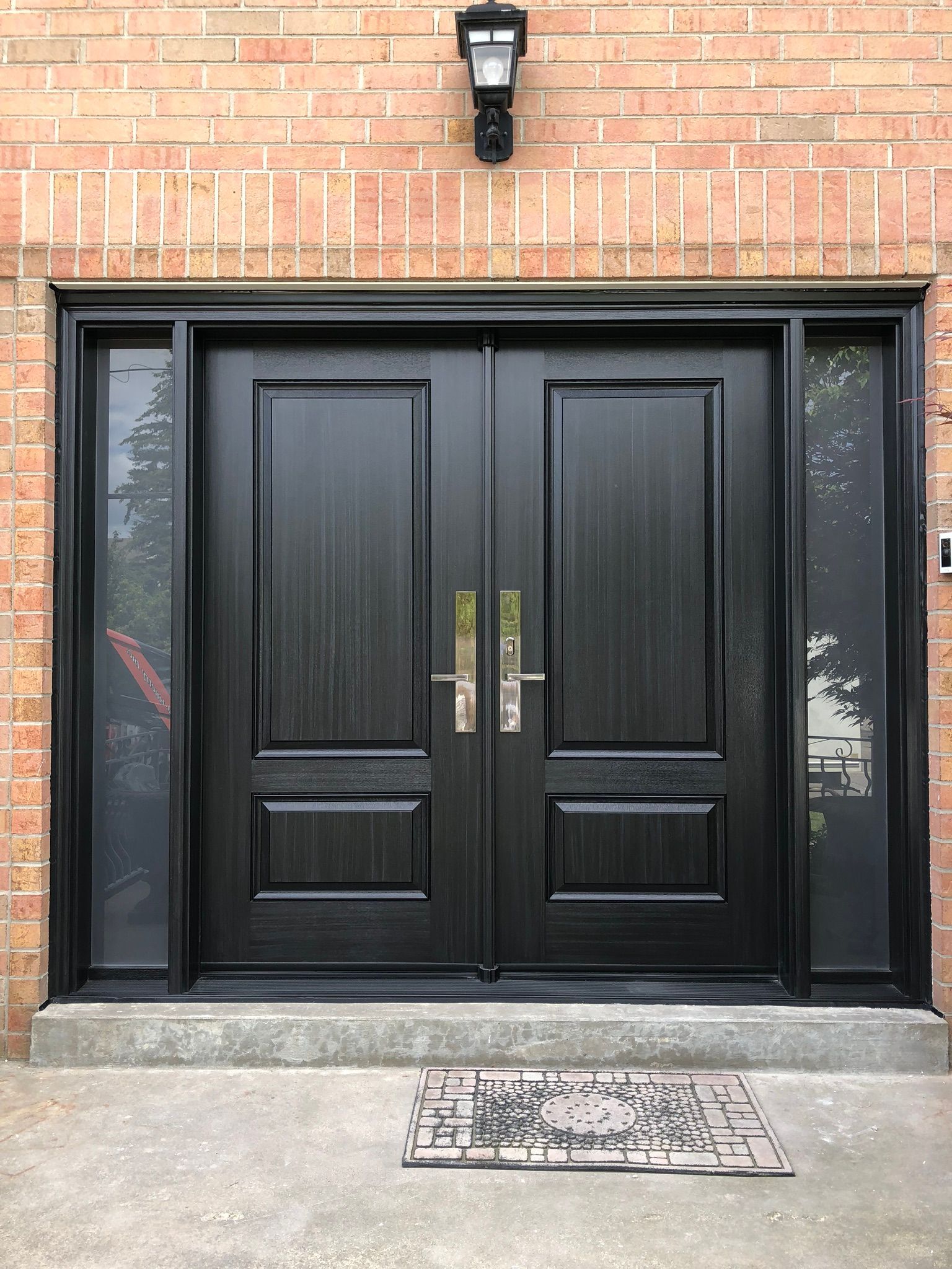 A black double door is sitting on top of a brick wall.