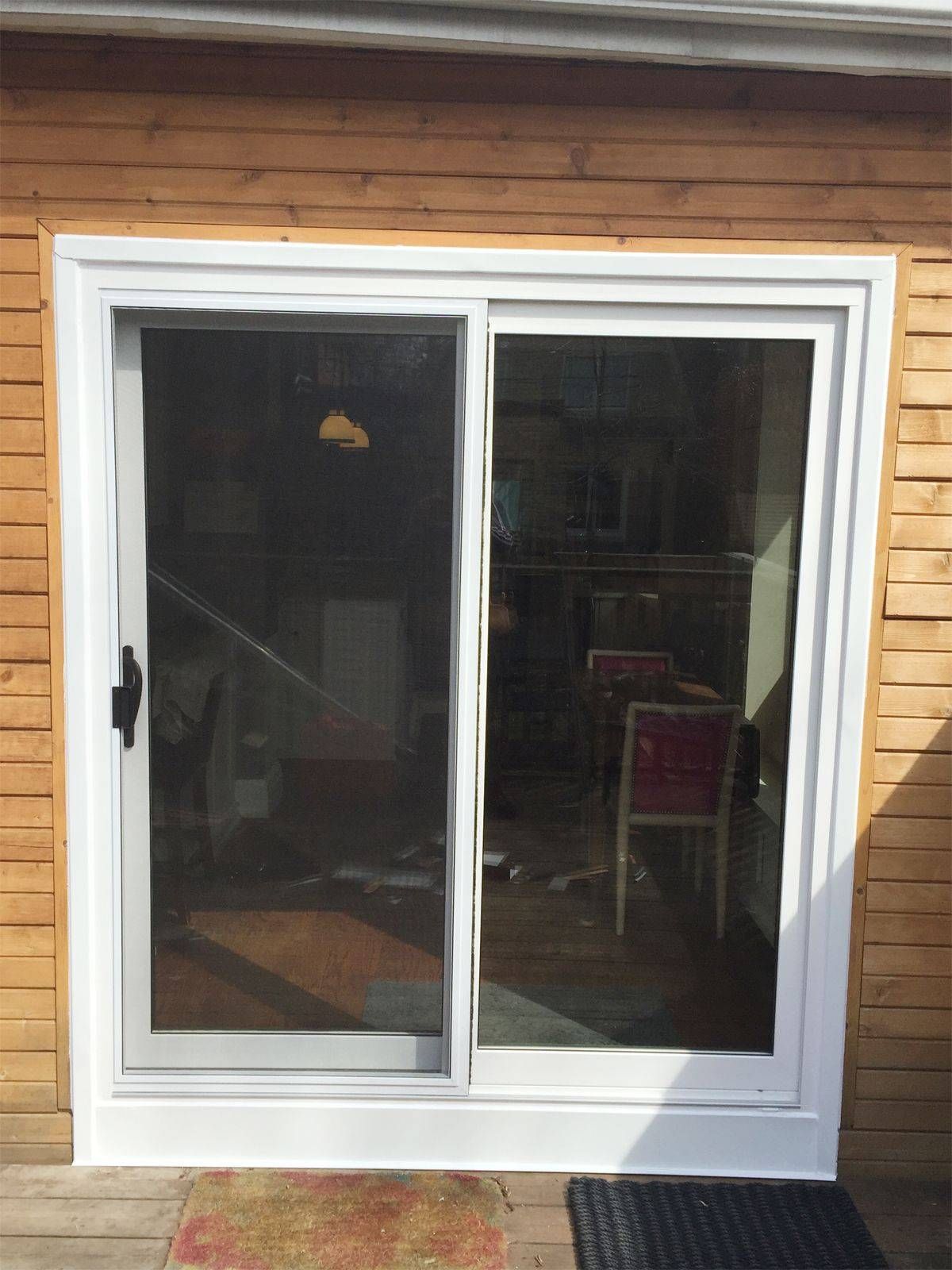 A white sliding glass door is sitting on the side of a wooden house.