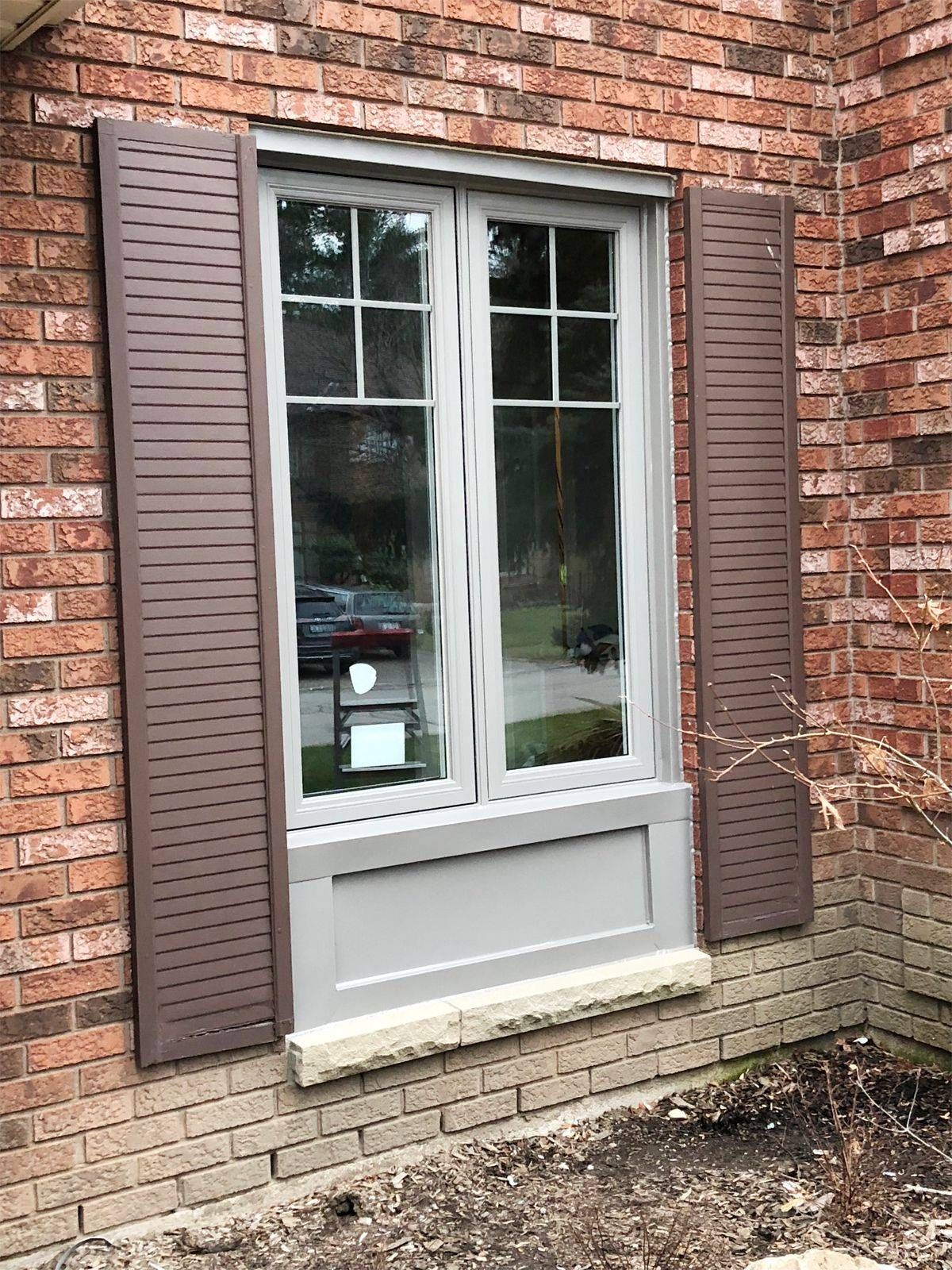 A window with brown shutters on a brick wall.