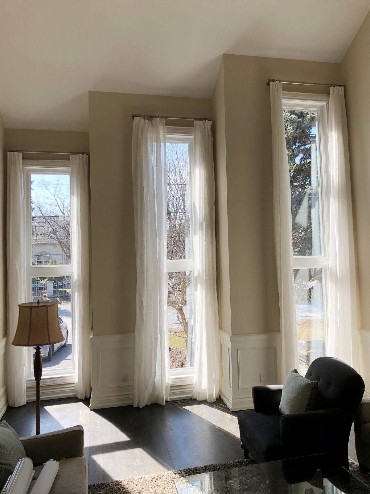 A living room with a couch , chair , lamp and two windows.