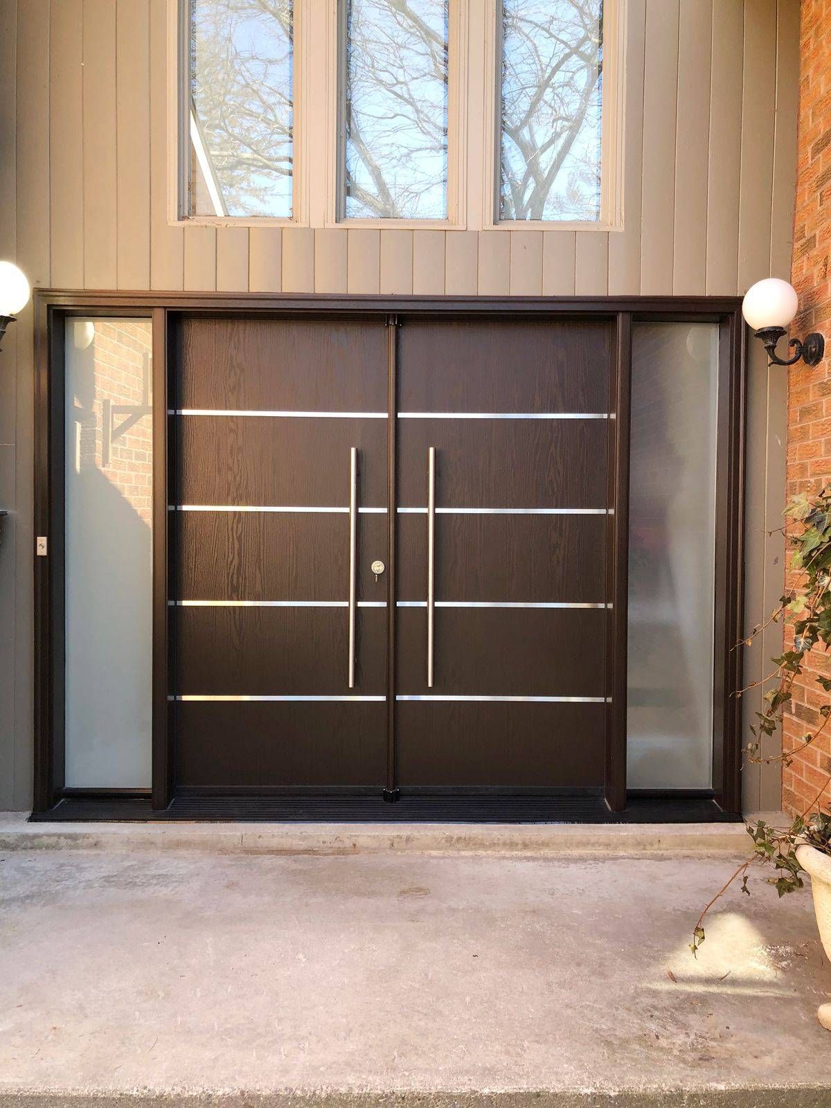 A large wooden door with stainless steel handles is sitting in front of a brick building.