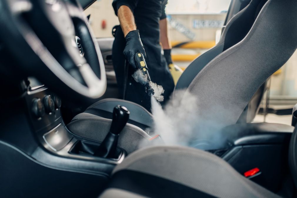 Persona che pulisce a vapore l'interno di un'auto, concentrandosi sui sedili, generando vapore visibile.