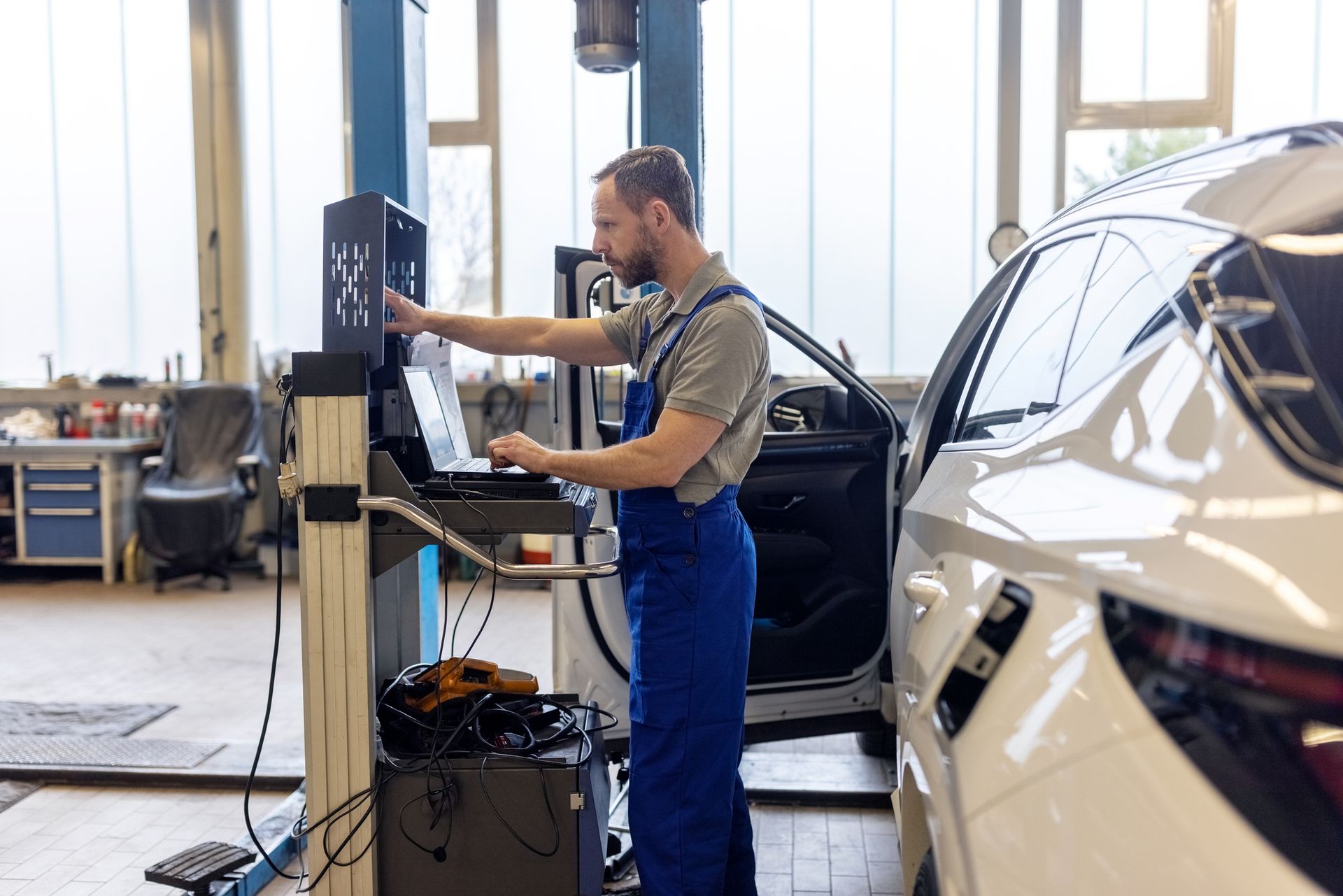 Un meccanico in tuta blu utilizza un computer diagnostico vicino a un'auto bianca in un'officina.