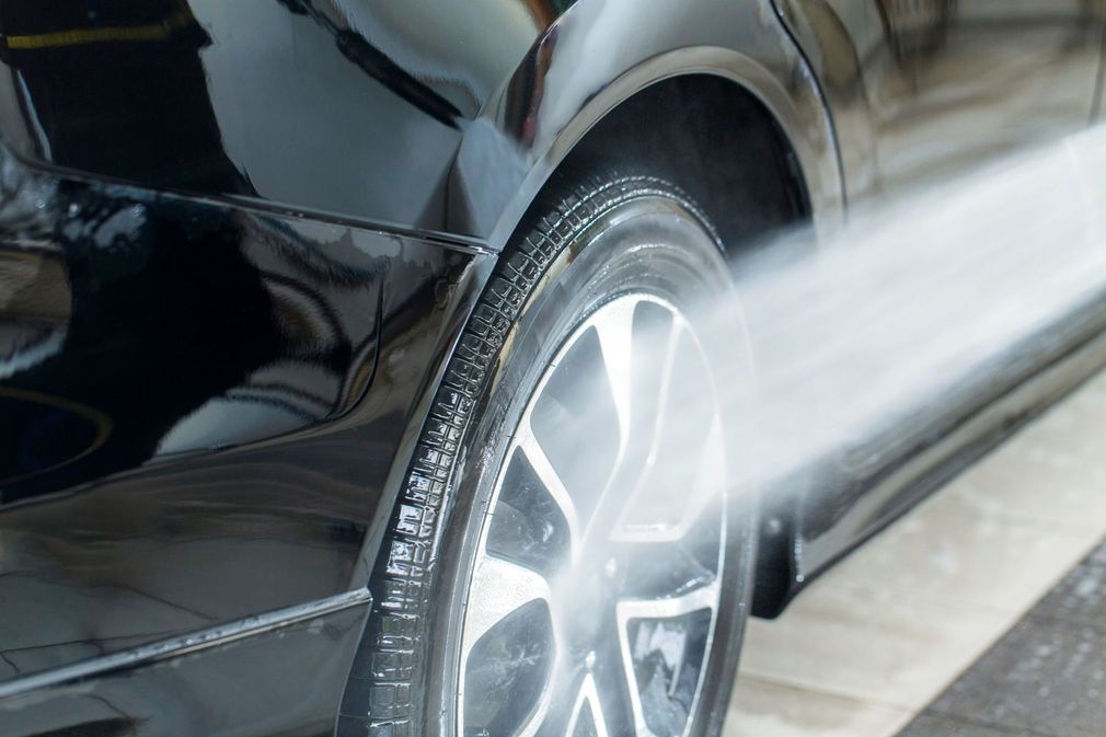 Un'auto nera viene lavata con un'idropulitrice, pulendo uno pneumatico e una ruota.