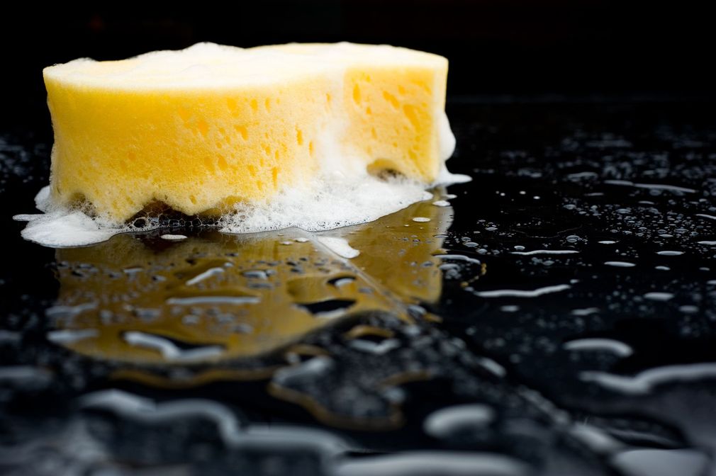 Spugna gialla su una superficie bagnata e scura, ricoperta di schiuma bianca.