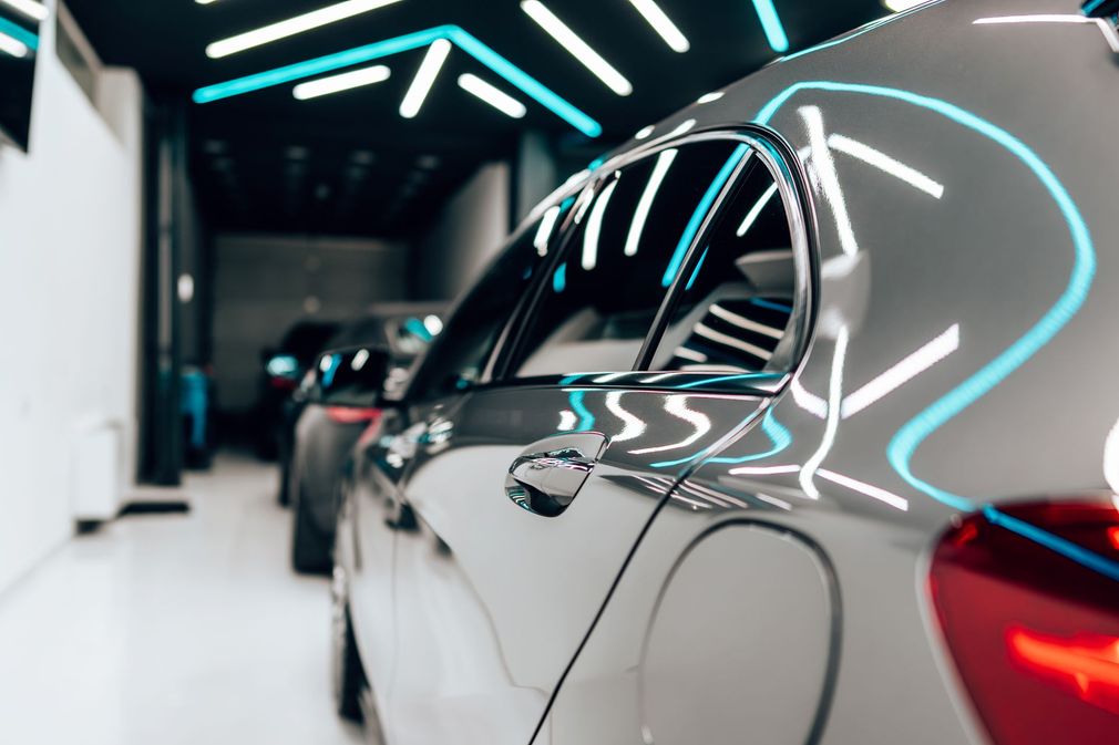 Un'auto color argento scintillante in uno showroom con luci blu e bianche che si riflettono sulla sua superficie lucida.