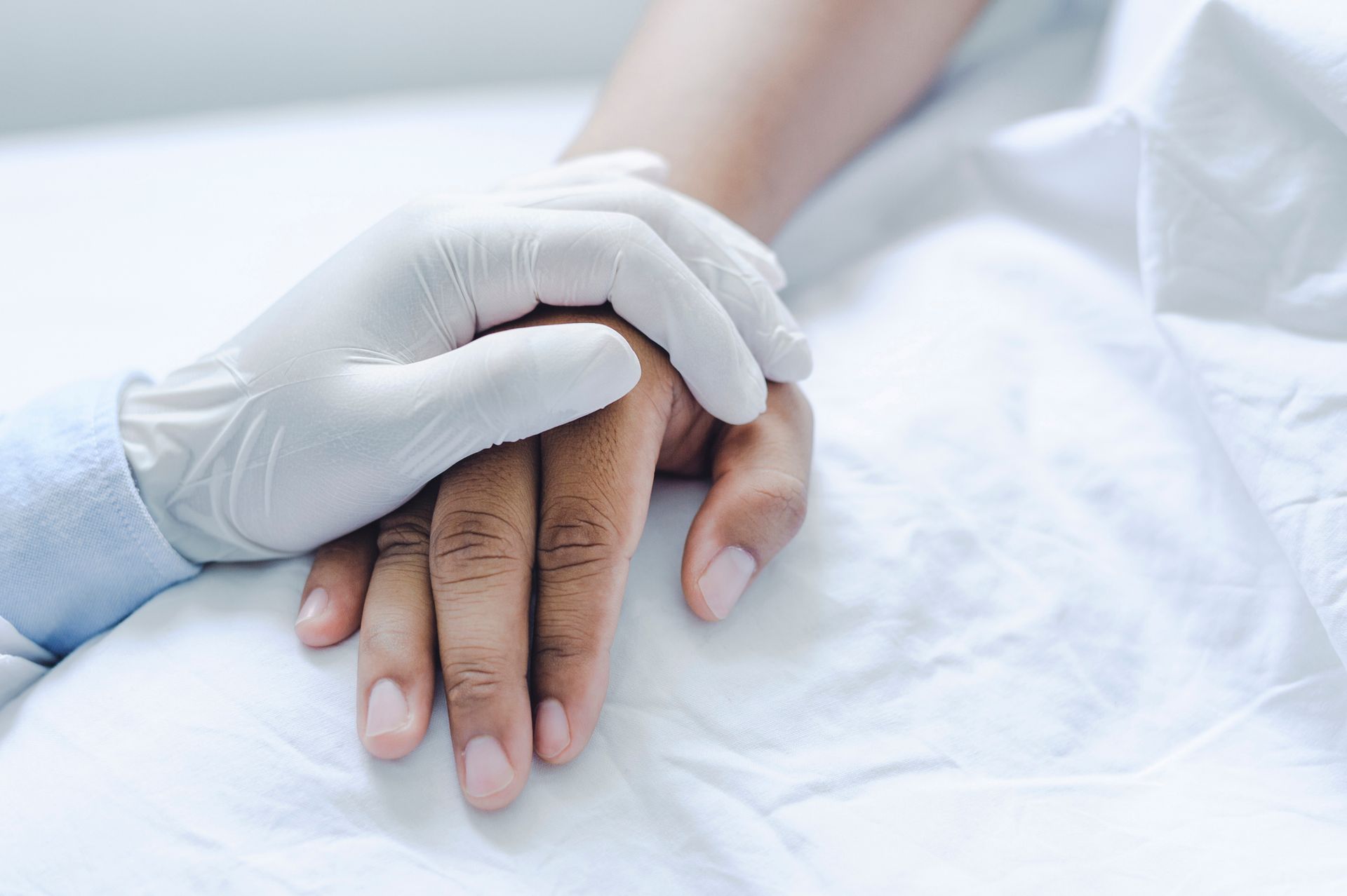 Um médico segura a mão de um paciente numa cama de hospital.