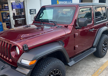 A maroon two-door Jeep Wrangler parked in front of a service center building with a key drop sign visible.