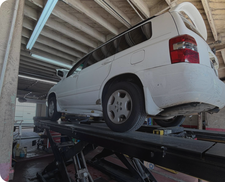 A white SUV is raised on a hydraulic lift inside an automotive repair shop.