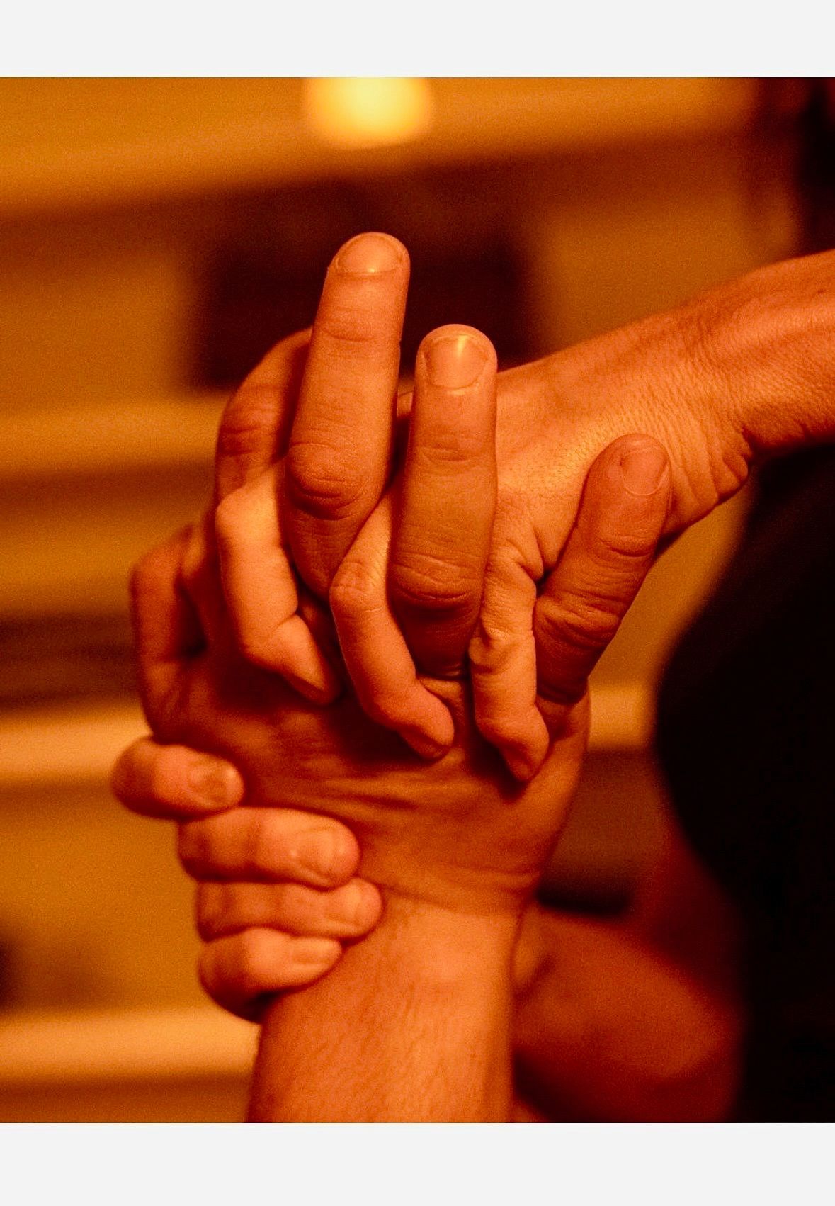 A close-up of a massage therapist performing a therapeutic back massage in a dimly lit, candlelit room.