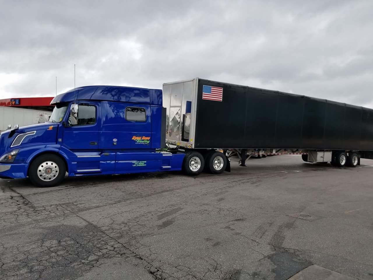 A blue semi truck with a black trailer is parked in a parking lot