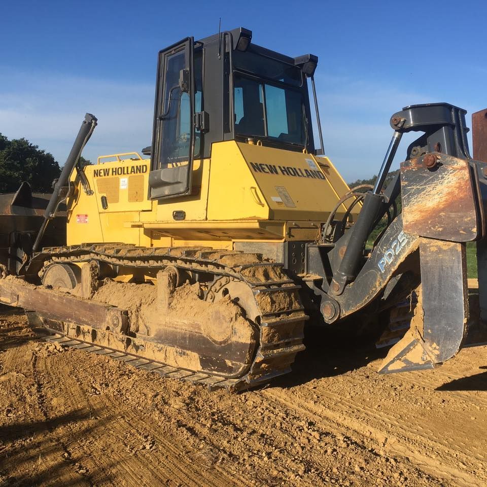 Bulldozer giallo New Holland su terra, con cingoli, lama e cabina, in un ambiente esterno.