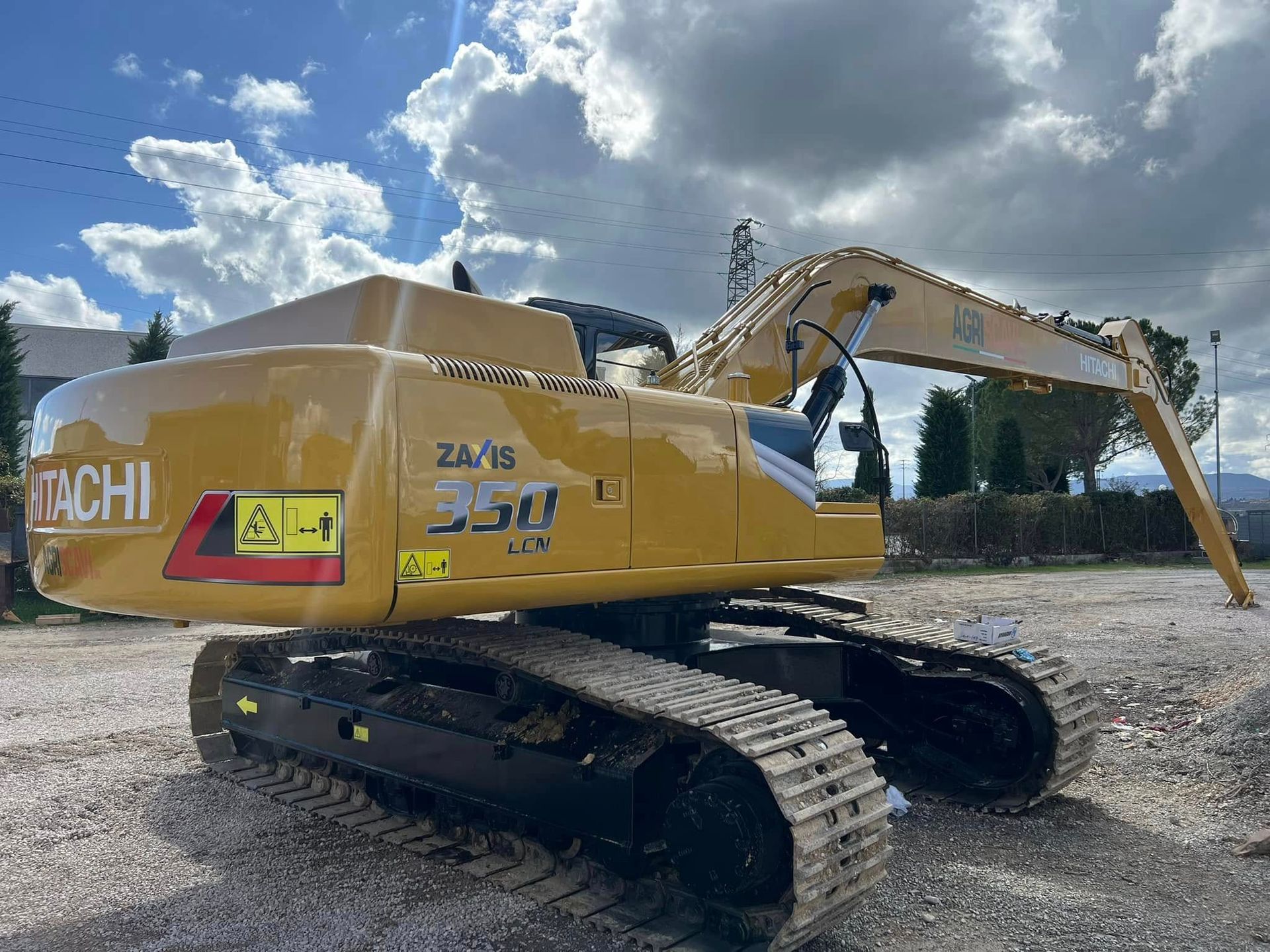 Escavatore Hitachi giallo su cingoli, parcheggiato all'aperto sotto un cielo nuvoloso.