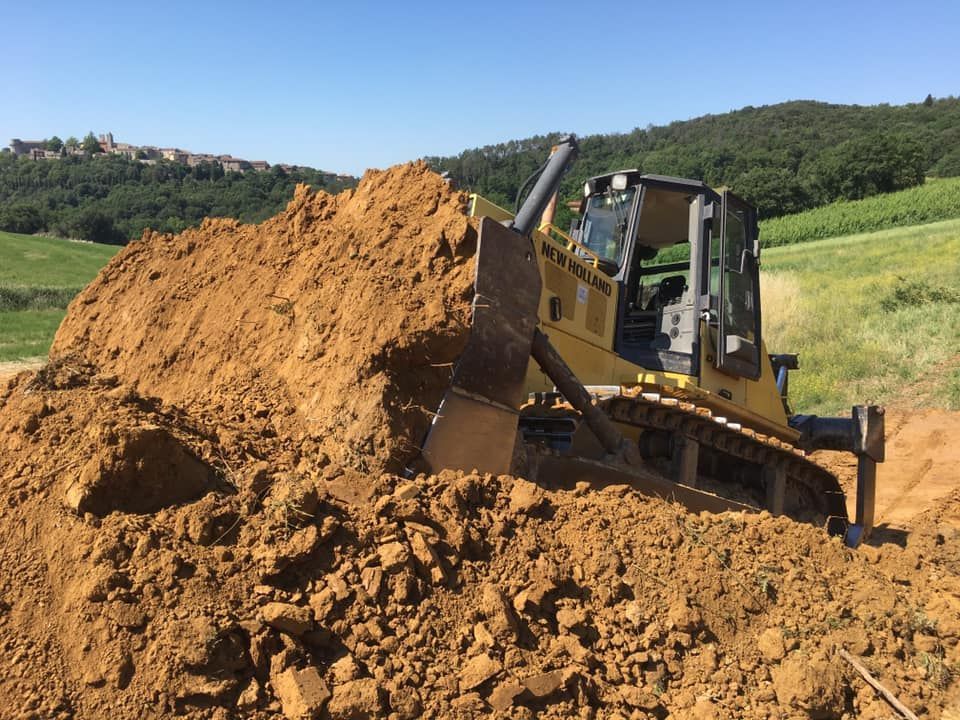 Un bulldozer giallo spinge terra marrone in una giornata di sole con una città sullo sfondo.
