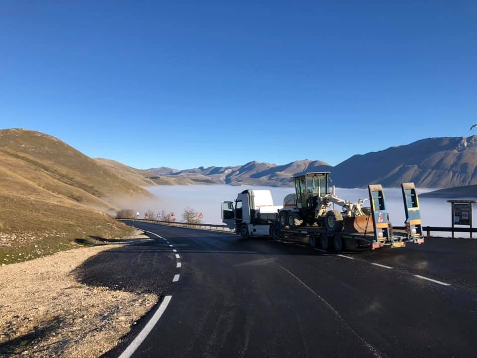 Camion che trasporta attrezzature edili su una strada di montagna sopra un mare di nuvole. 