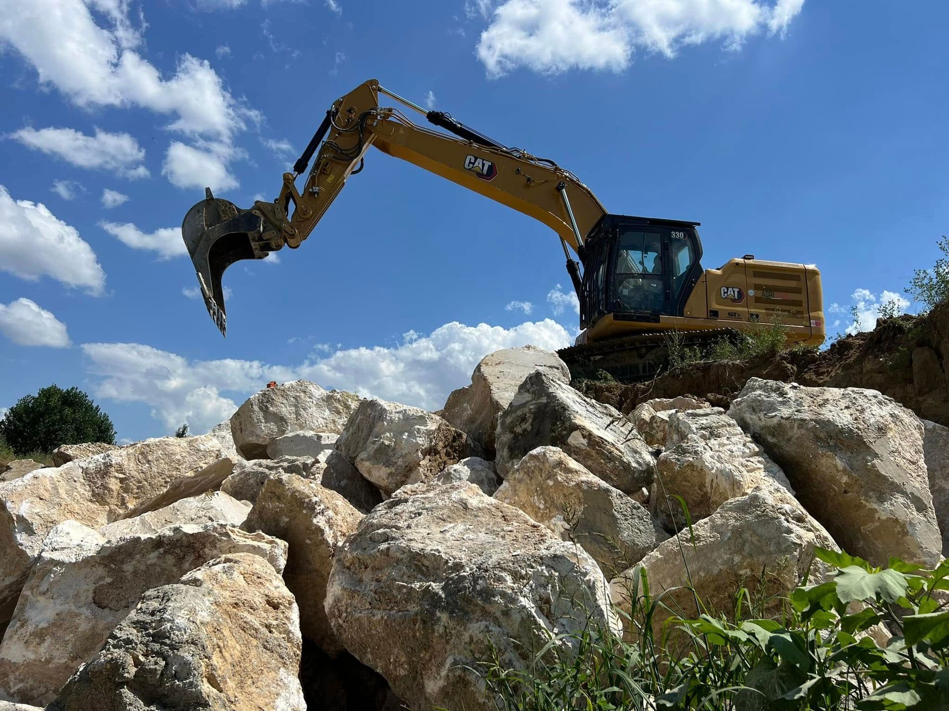 Escavatore giallo su un mucchio di grandi rocce bianche sotto un cielo azzurro.