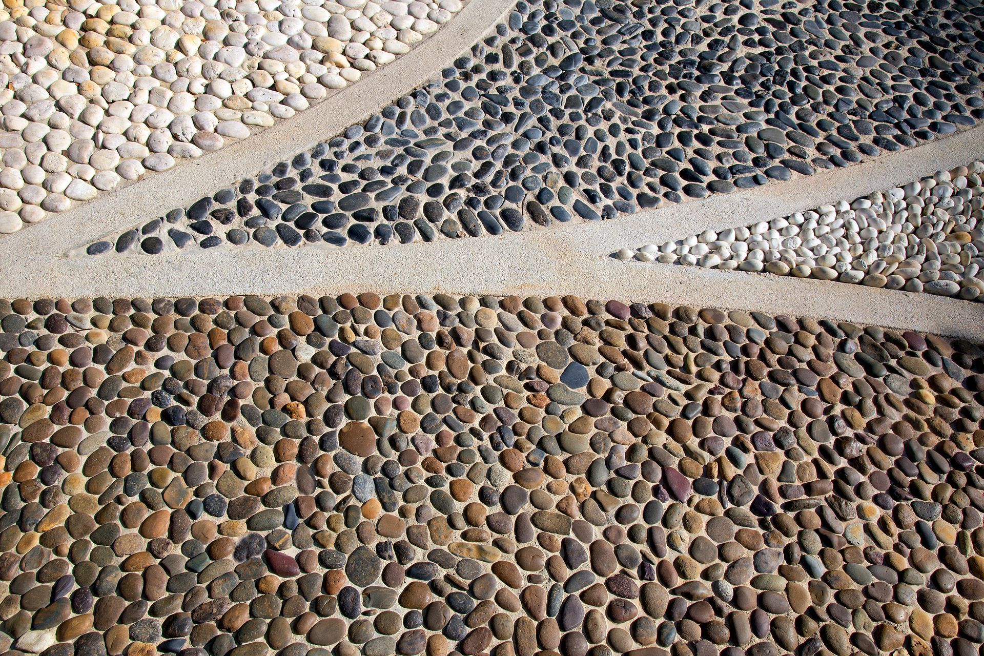 Passerella in mosaico di ciottoli con sezioni di pietre bianche, nere e marroni, divise da cemento.