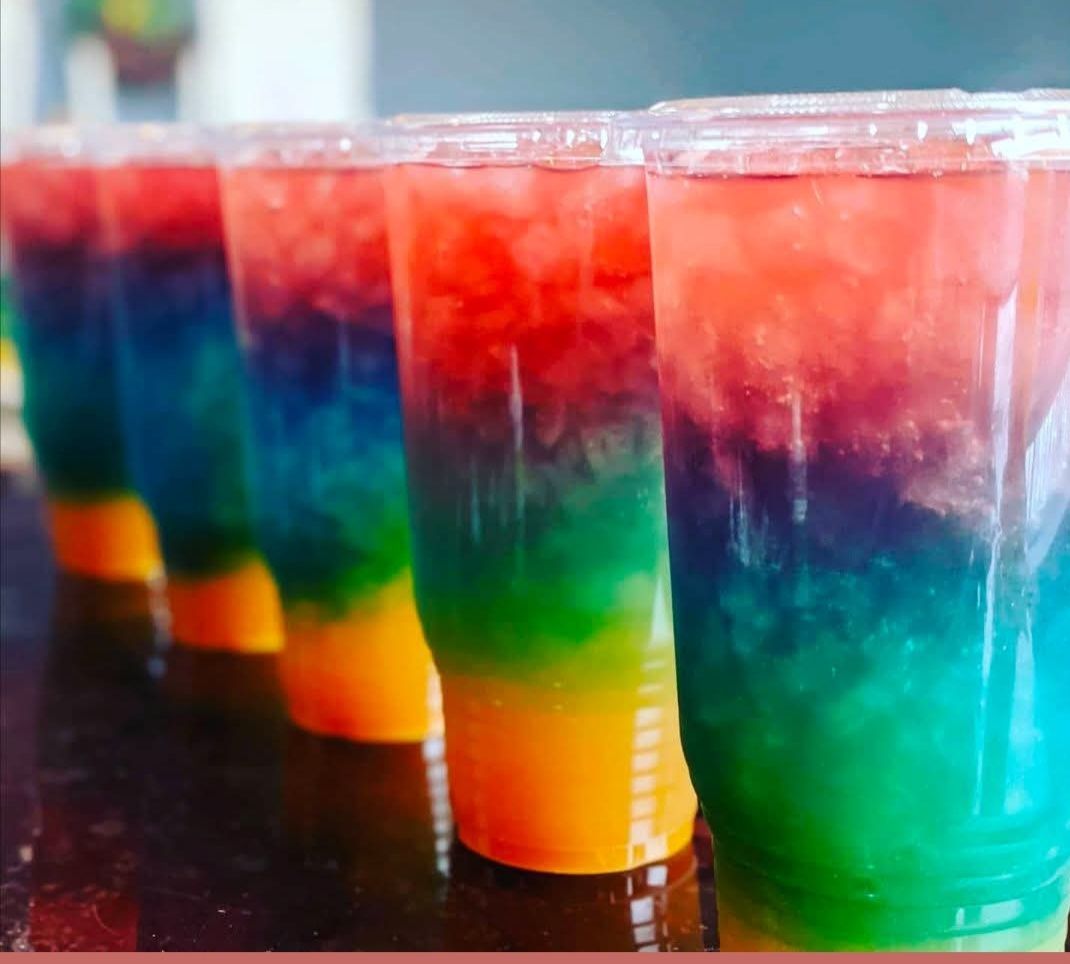 Two glasses of different colored drinks with straws on a table.