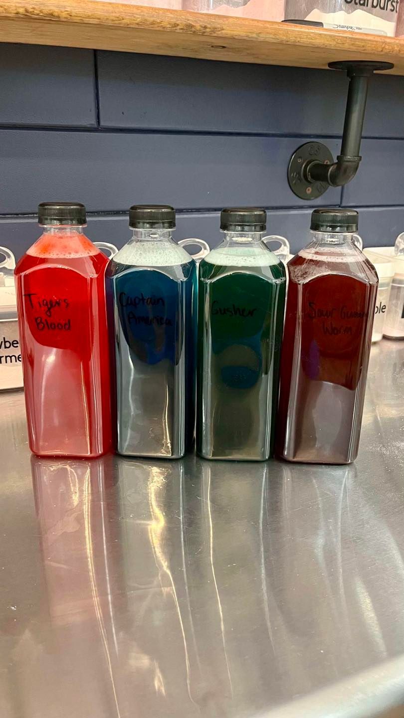 Three glasses of different colored drinks with mint leaves on a table.