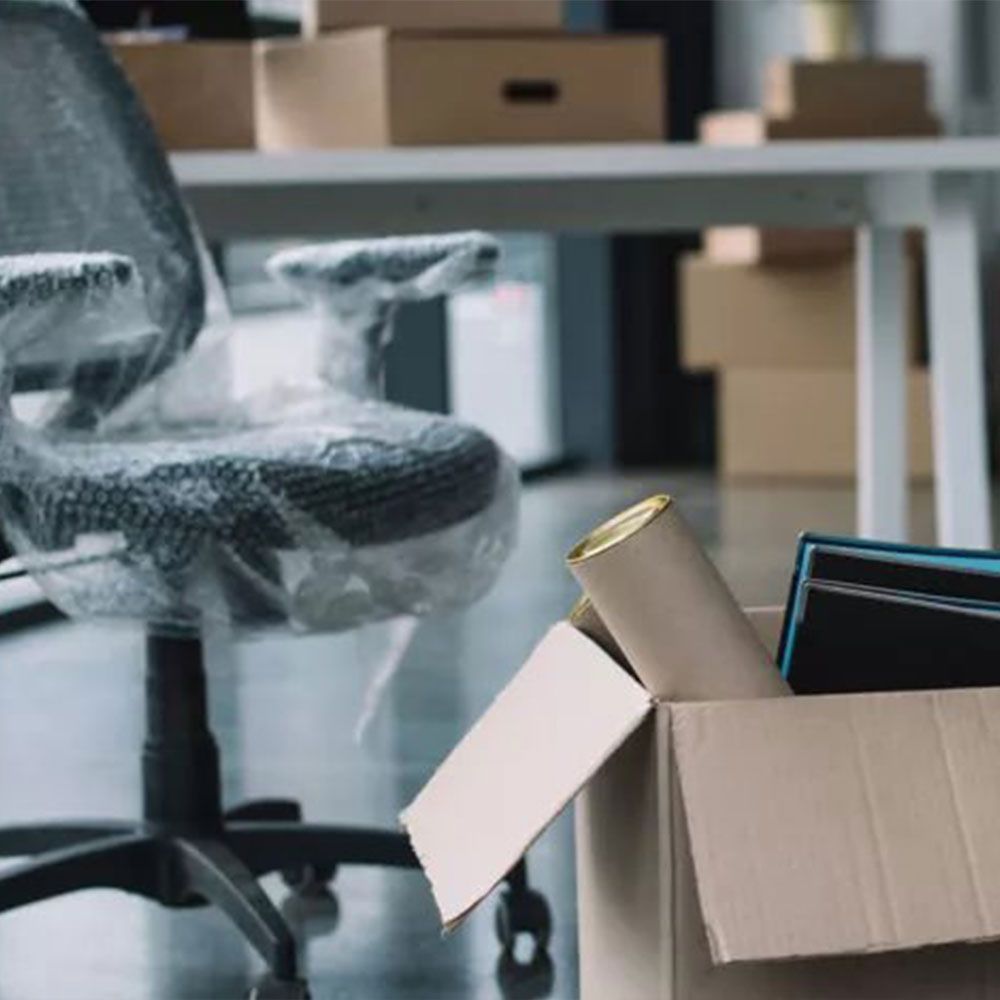 A cardboard box filled with books and a roll of tape is in an office.