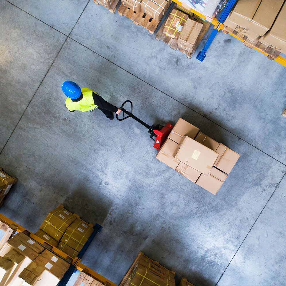 An aerial view of a man pushing a pallet truck full of boxes in a warehouse.