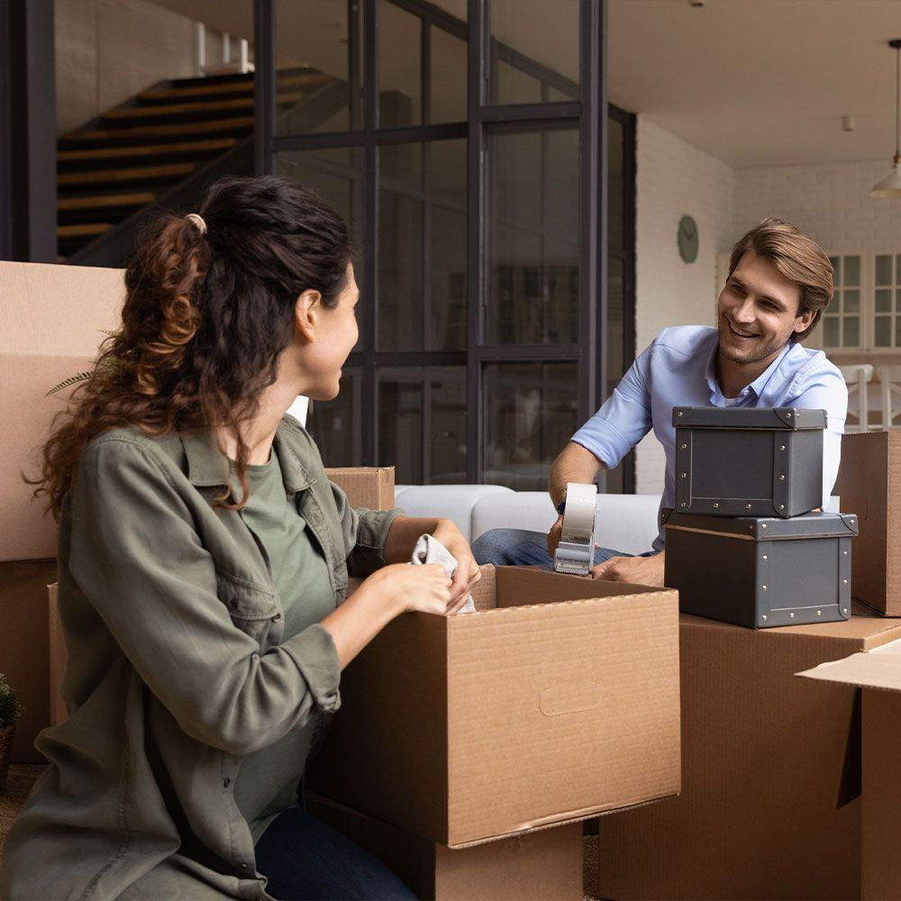 A man and a woman are sitting on a couch surrounded by cardboard boxes.