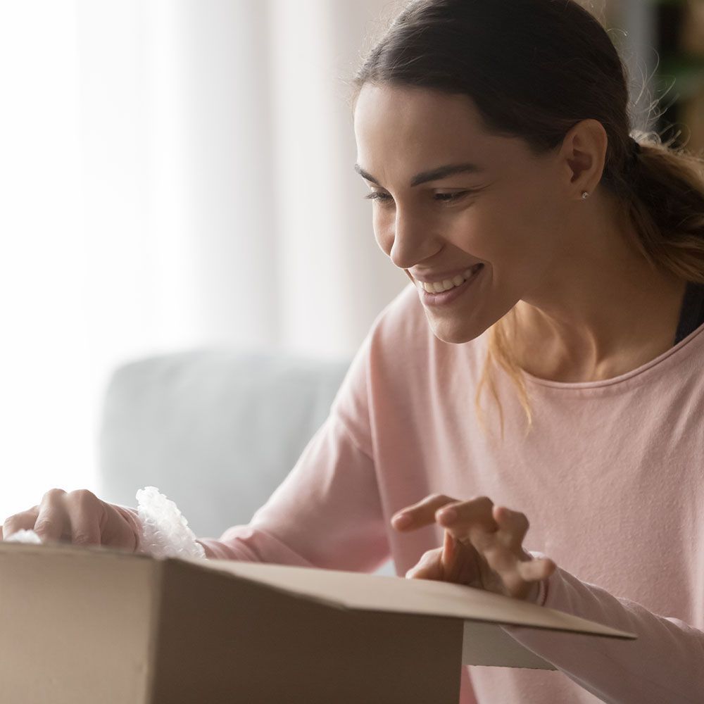 A woman is smiling while opening a cardboard box.