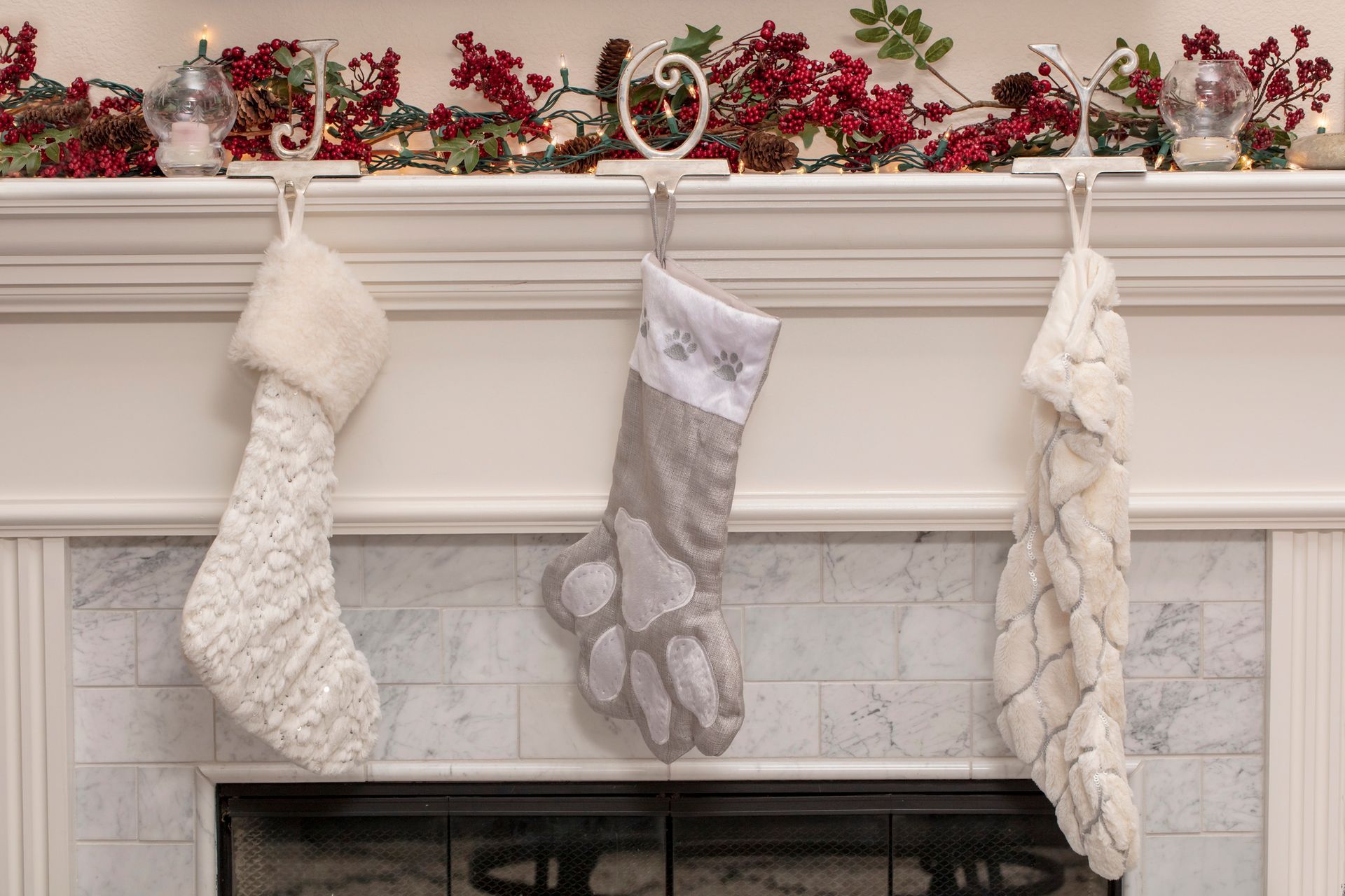 Three Christmas stockings hanging above a fireplace, decorated with garland and berries.
