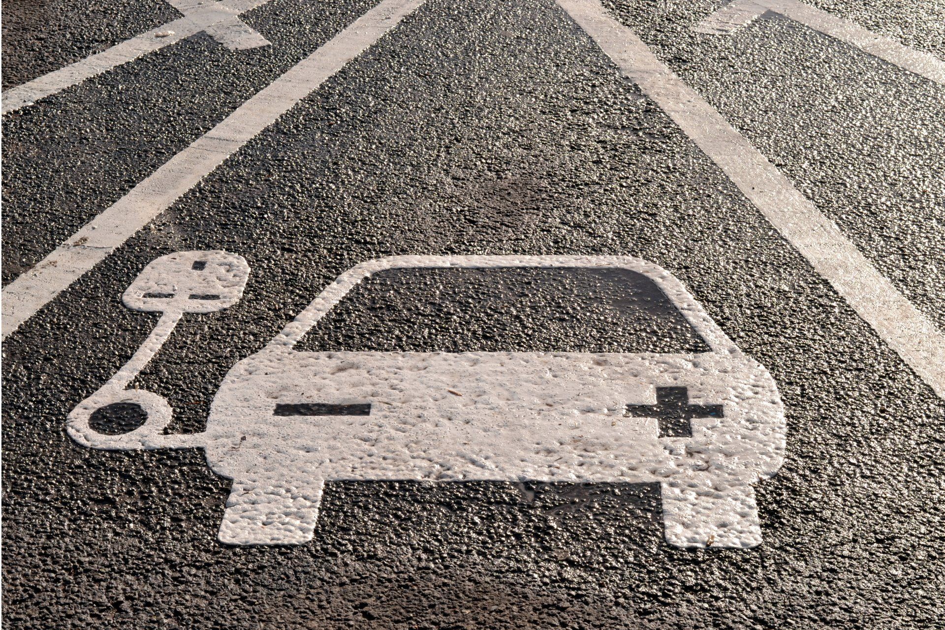 White EV charging icon on asphalt parking space