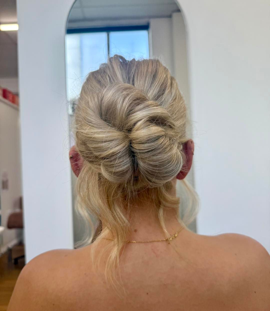 Back view of blonde hair in a twisted low bun, showing the neck and shoulders in a salon mirror — Pose Hair Design in Orange, NSW