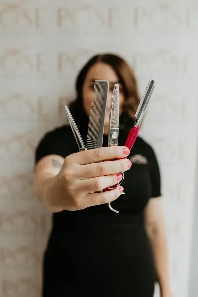 Hand Holding Combs and Scissors in Front of A Blurred Salon Backdrop — Pose Hair Design in Orange, NSW
