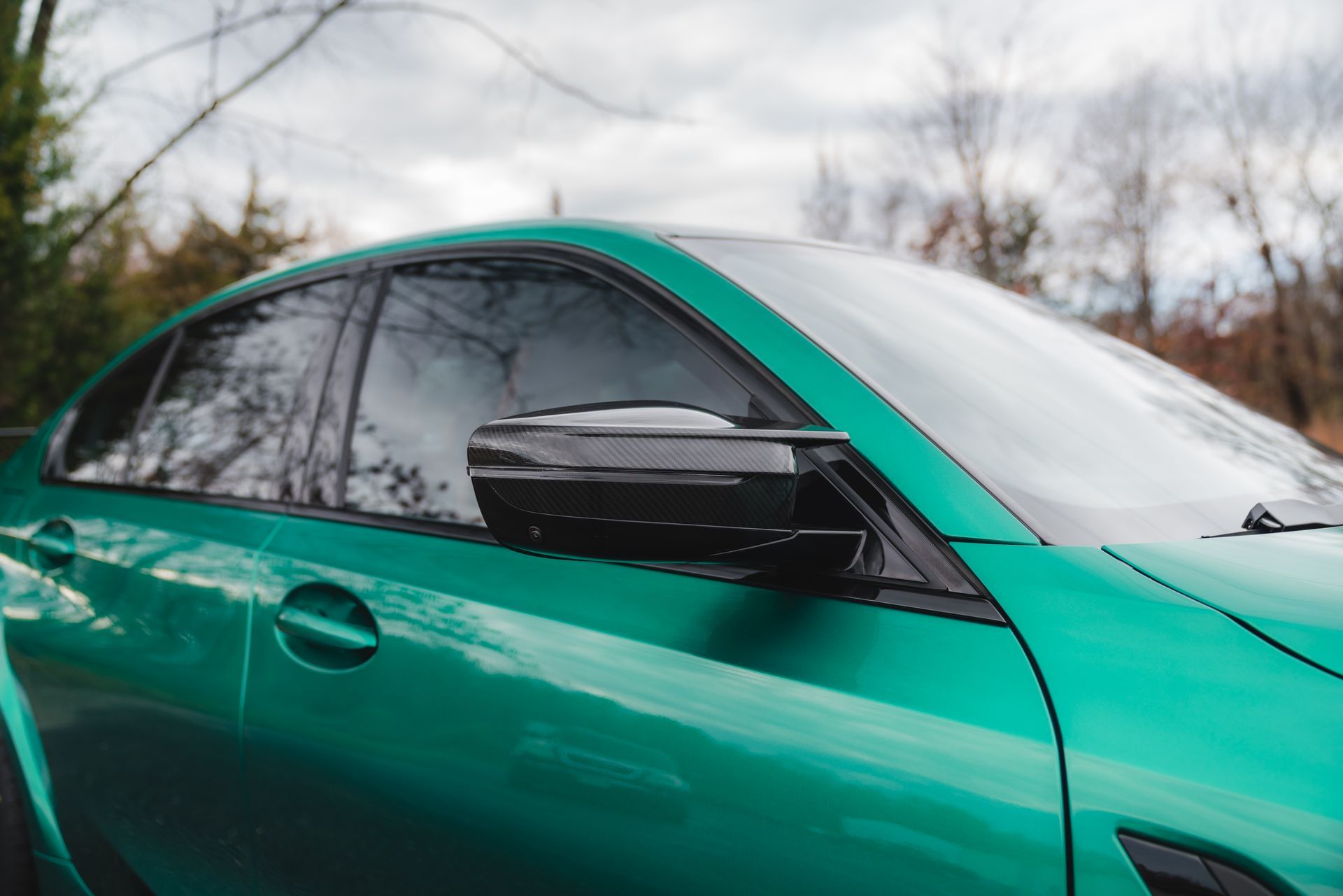 A green bmw m3 is parked in front of a forest.