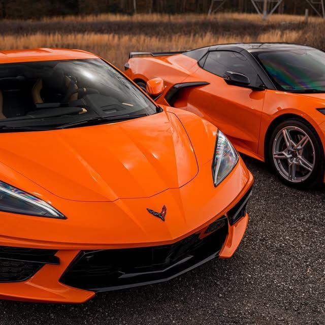 Two bright orange Chevrolet Corvette sports cars parked on asphalt.