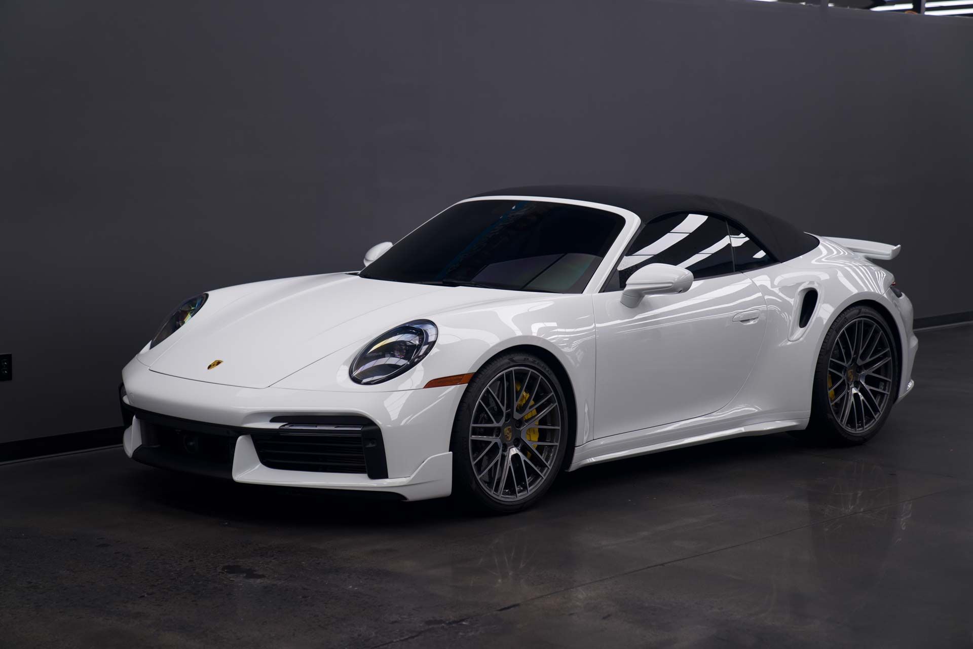 A white porsche 911 turbo s convertible is parked in a showroom.