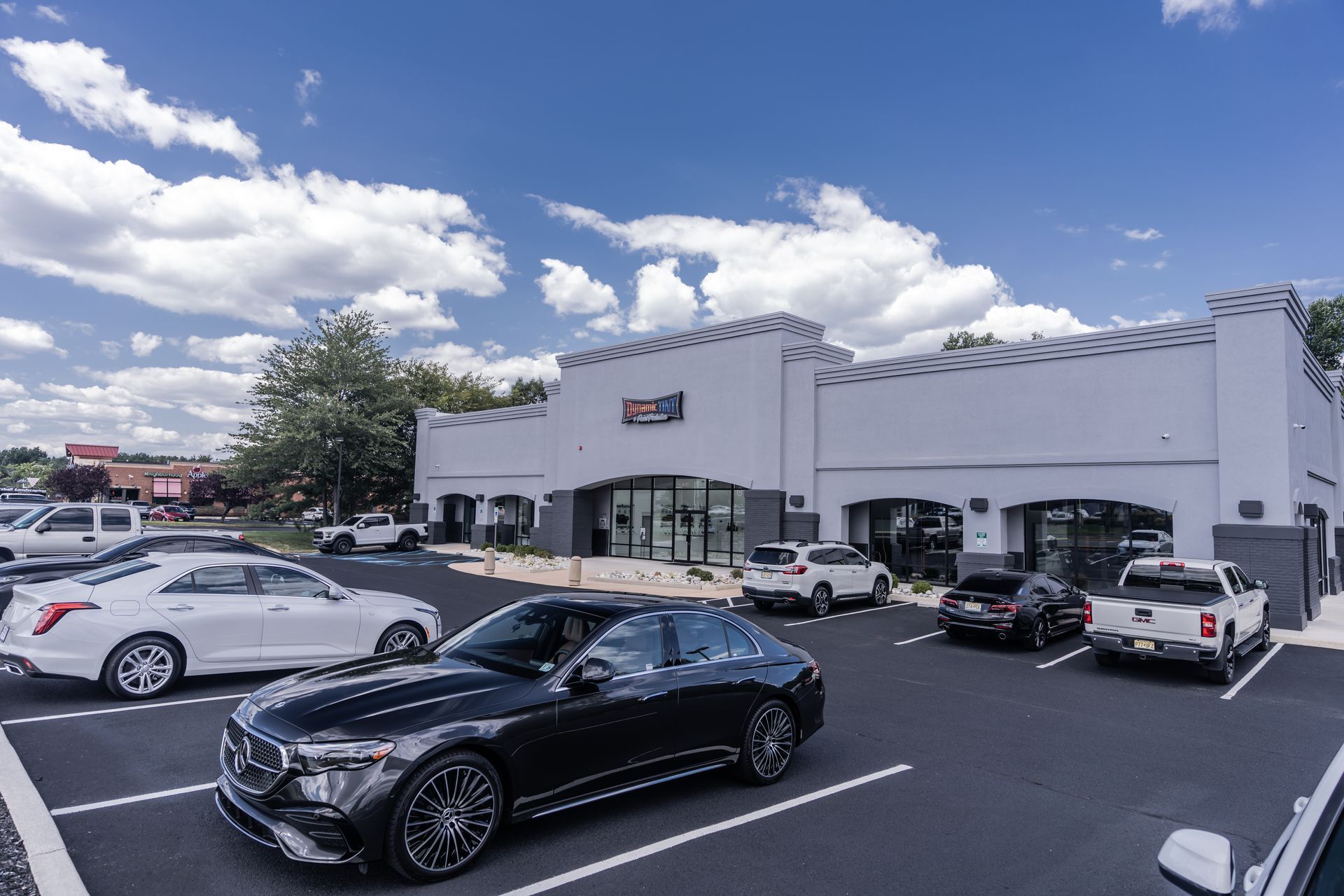 Cars parked in front of a modern, gray building with glass doors and a blue sky.