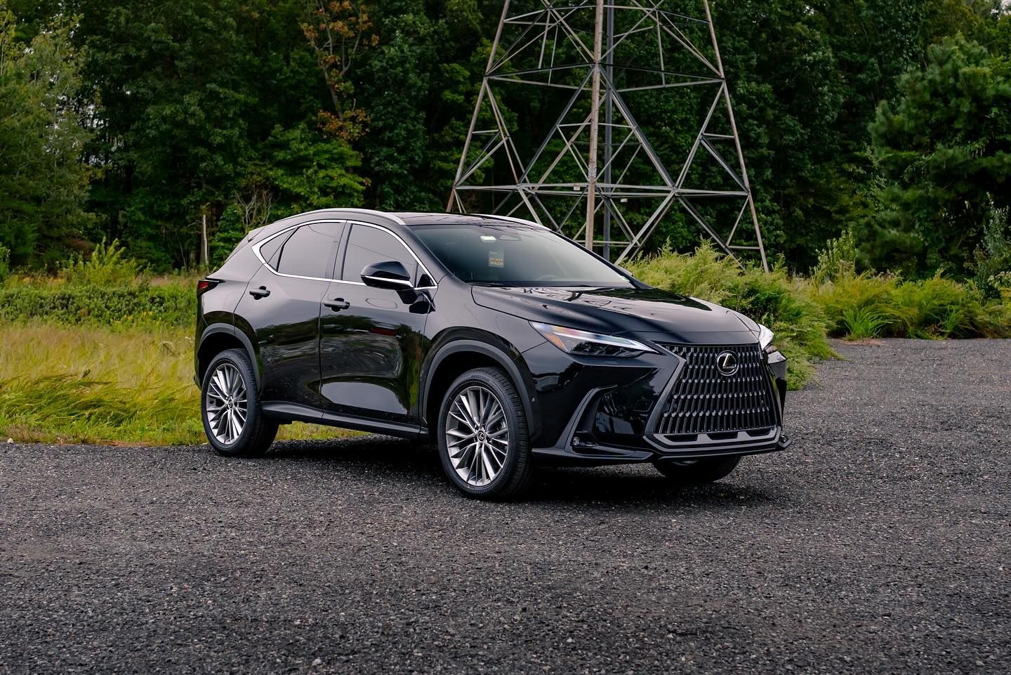 Black Lexus SUV parked on gravel with trees and a utility tower in the background.