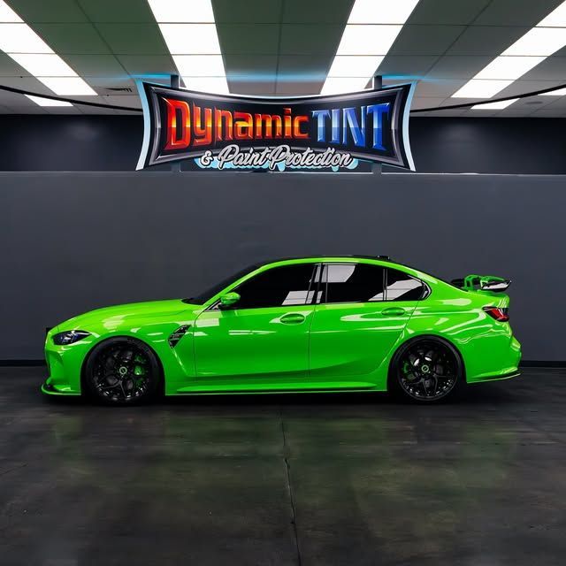 Green BMW car, tinted windows, black wheels, under "Dynamic Tint & Paint Protection" sign.
