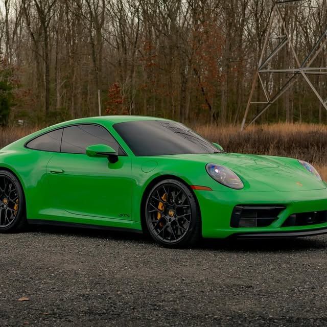 Green Porsche sports car parked on a gravel road with trees in the background.