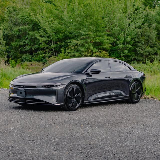 Dark gray Lucid Air electric sedan parked on asphalt with green trees in the background.