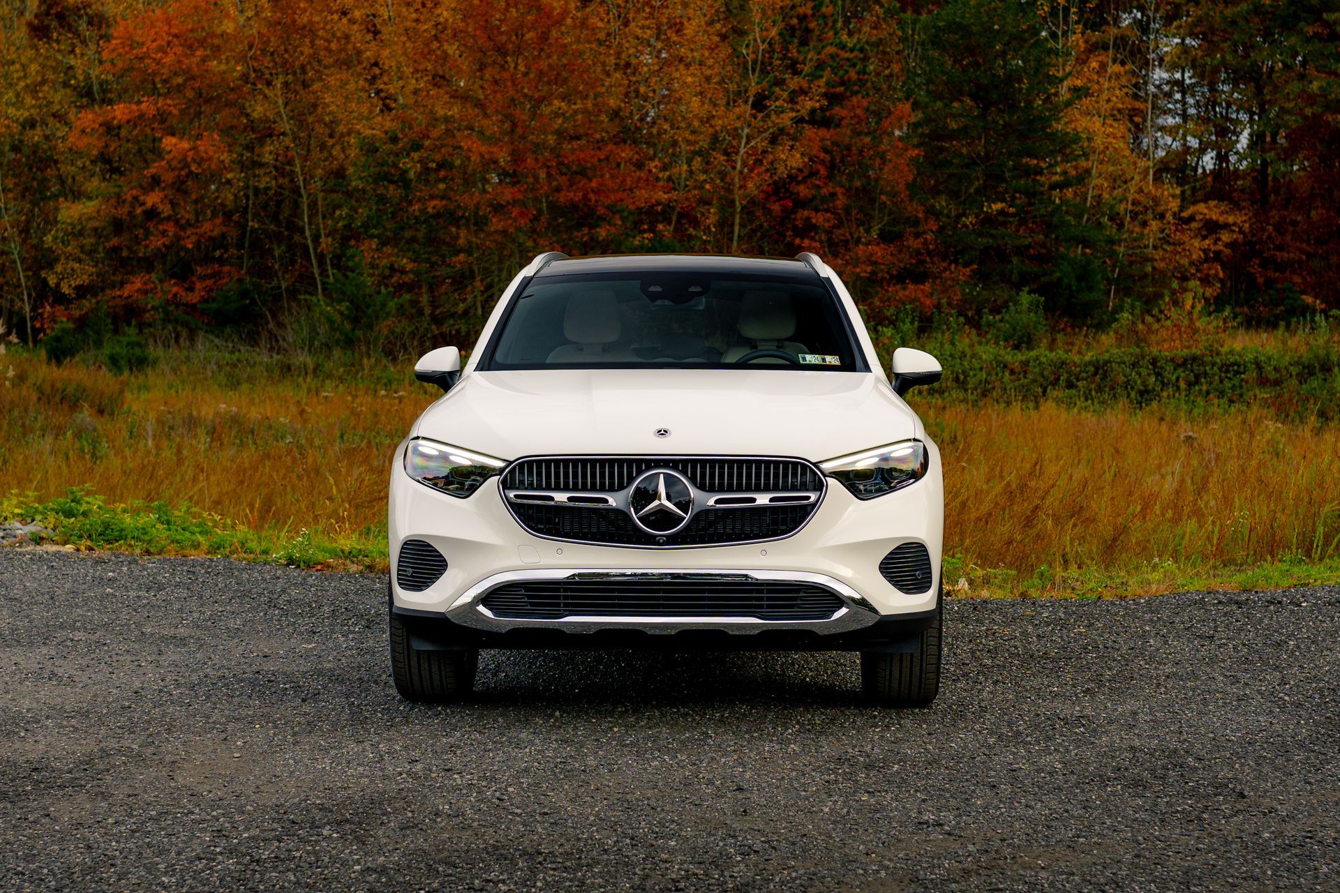 A white mercedes benz suv is parked on a gravel road in front of a field.