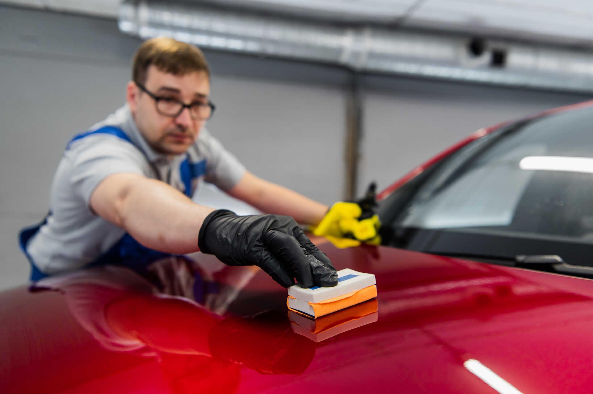 A man is polishing the hood of a red car.