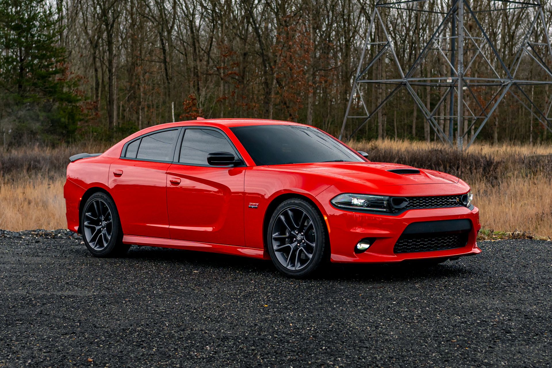 Red Dodge Charger parked on gravel with a forest background.