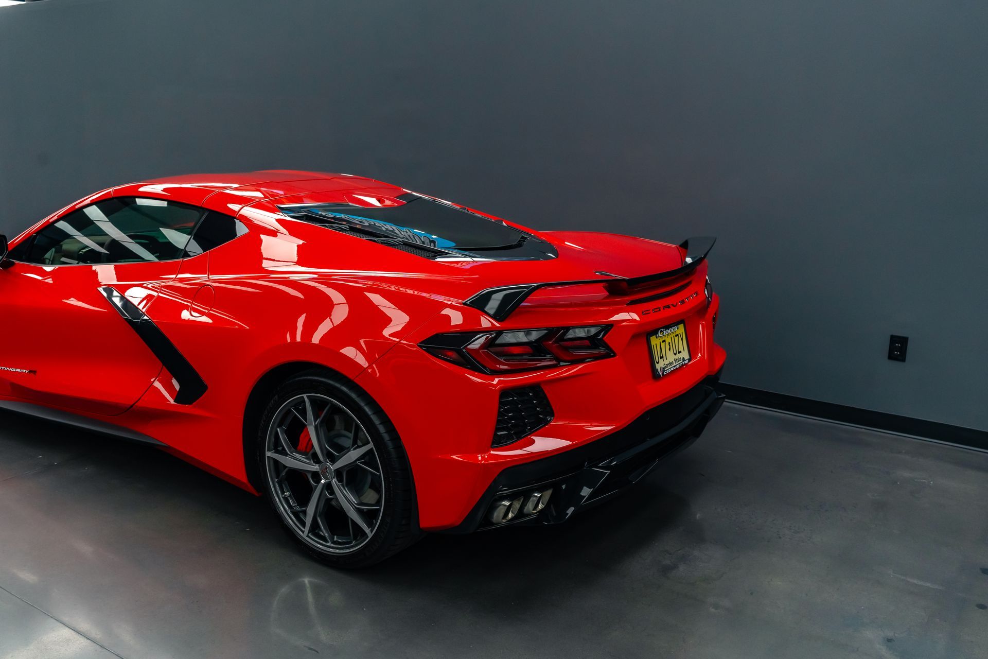 A red sports car is parked in a garage next to a wall.