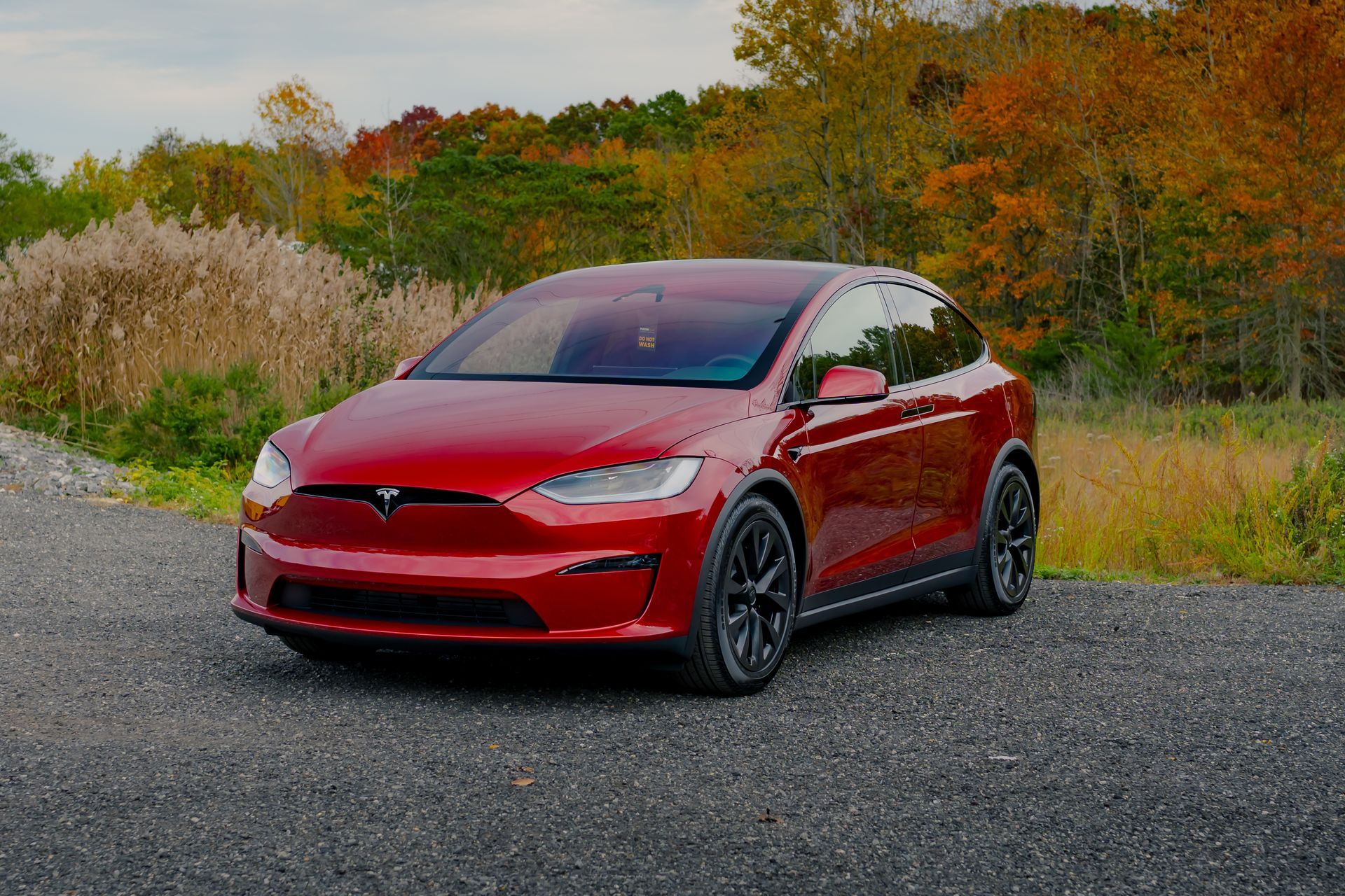 A red tesla model x is parked on the side of a gravel road.