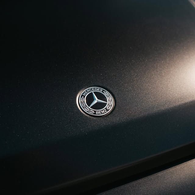 Mercedes-Benz emblem on a matte black car hood, metallic silver logo with a three-pointed star.
