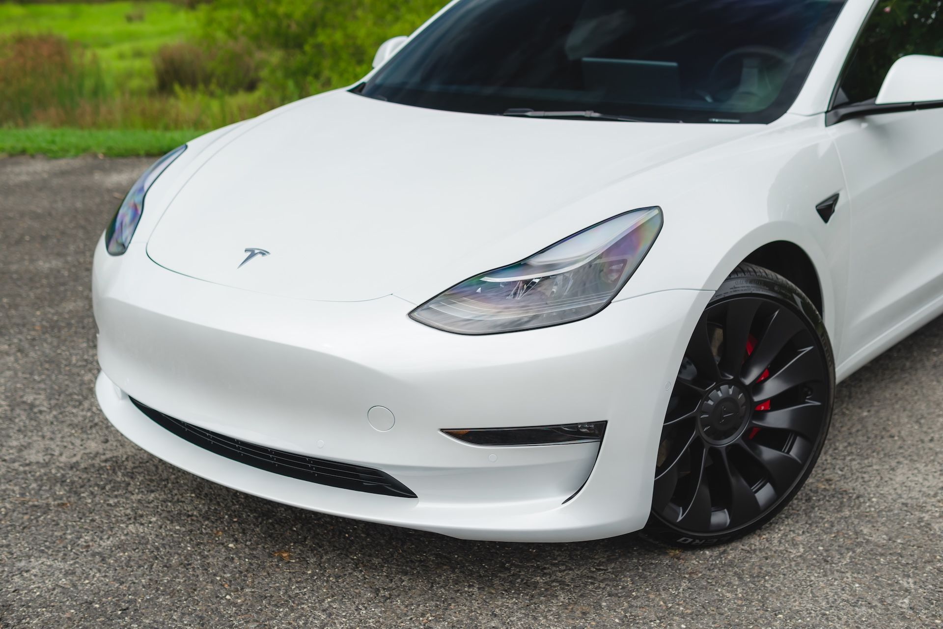 A white tesla model 3 is parked on a gravel road.
