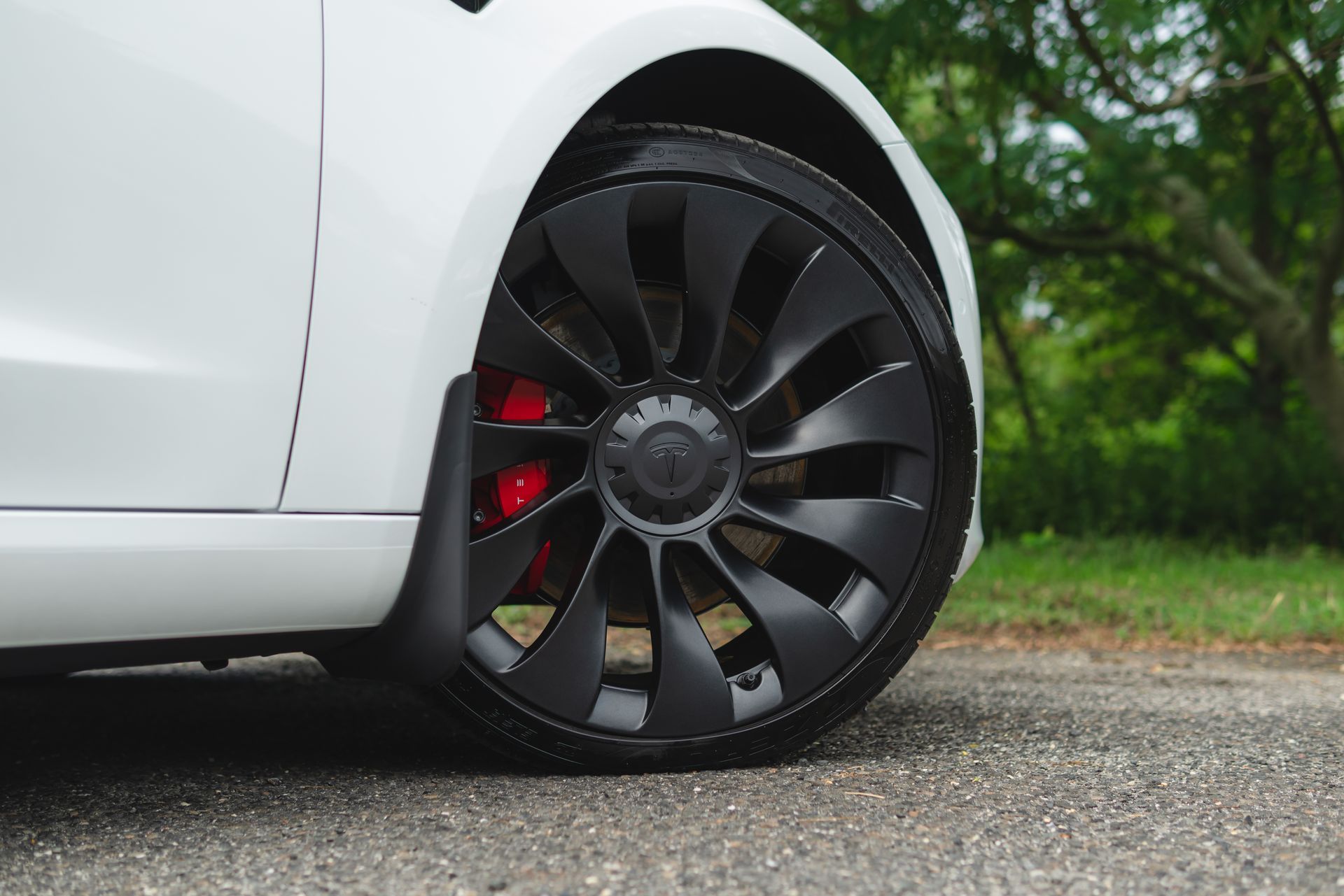 A white tesla model 3 with black wheels and red brake calipers is parked on the side of the road.