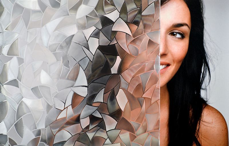 Woman smiling, partially obscured by patterned, decorative window film.